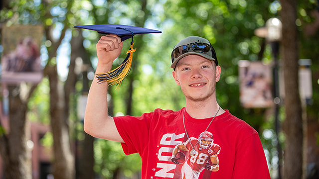 Spencer Nemecek holding up a J C C C graduation cap.