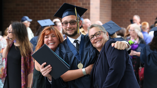 JCCC student at graduation hugging two faculty members