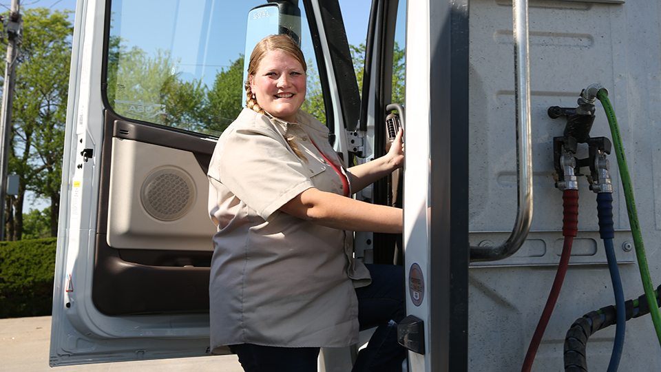CDL student Alison Smith stands next to a semi-truck cab.