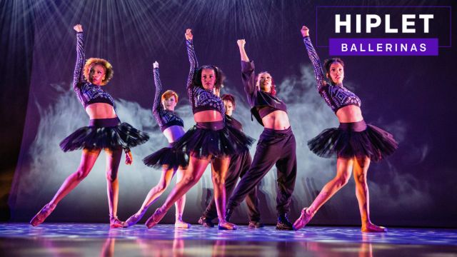 Six members of Hiplet Ballerinas of Chicago pose on stage with one arm raised in the air. They are wearing black and the stage is foggy.