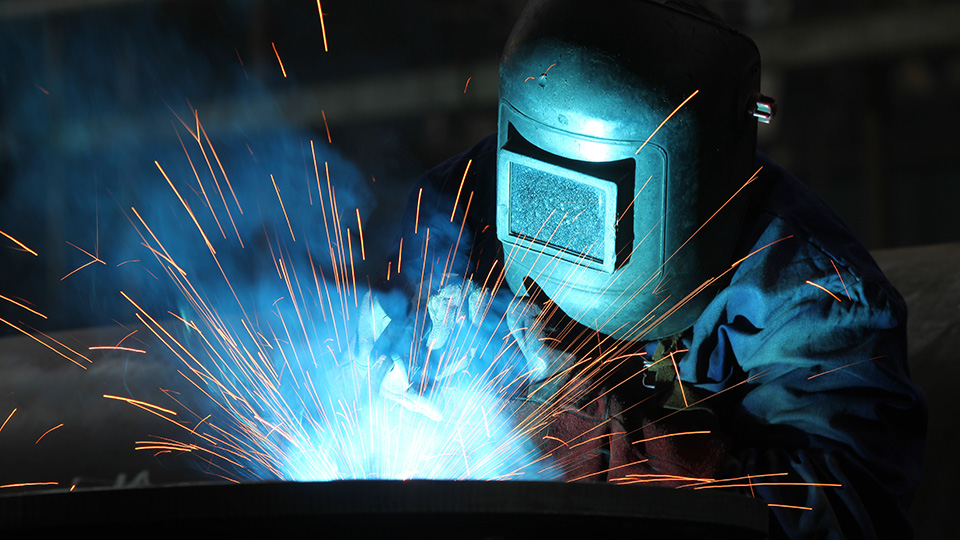 A person wearing a welding helmet makes sparks while welding.