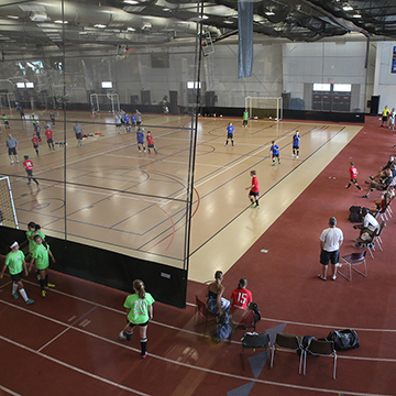 The JCCC gymnasium as seen from the bleachers. Teams play court games while others walk along the track.