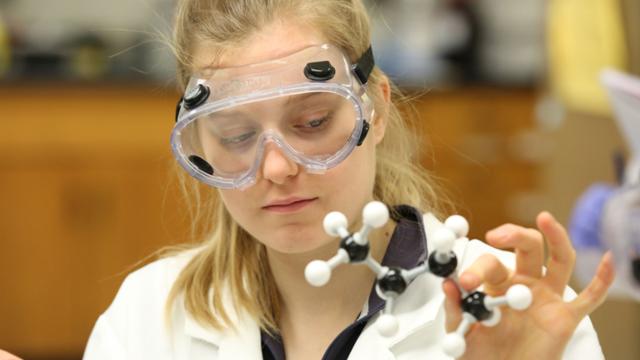 Young girl wearing safety goggles and holding a molecular model