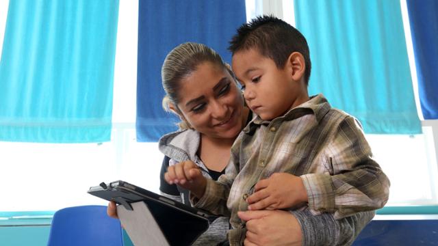 Mother sitting with son on her lap. The child is looking at a laptop on his lap.