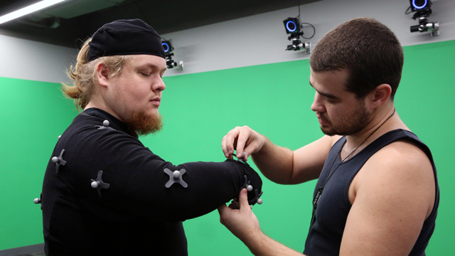 One student applying sensors to the arm of another student as they work in the motion capture studio
