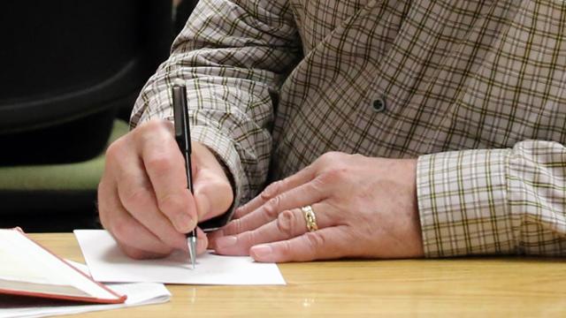 Close up of man's arms. He is sitting at a table writing in a notebook