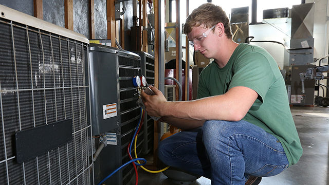 A young man who completed his Heating, Ventilation and Air Conditioning (HVAC) certificate at JCCC checks the settings on an HVAC system.