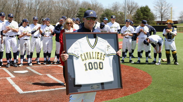 Coach Kent Shelley posing with a framed JCCC baseball jersey with the number 1,000 on it.