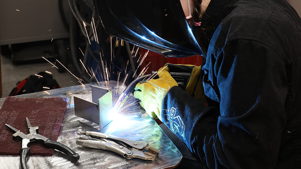 A jccc student wearing safety gear practices a weld in the lab