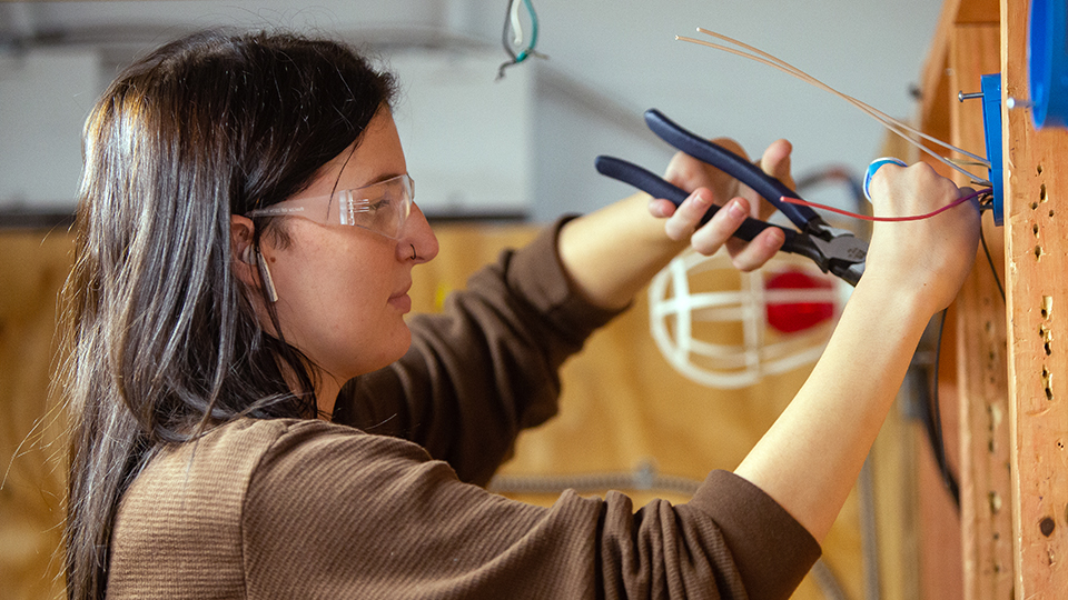 a woman in safety glasses works on wiring