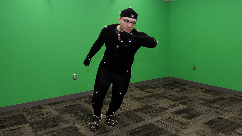 Student standing in front of a green screen wearing a suit that captures motions