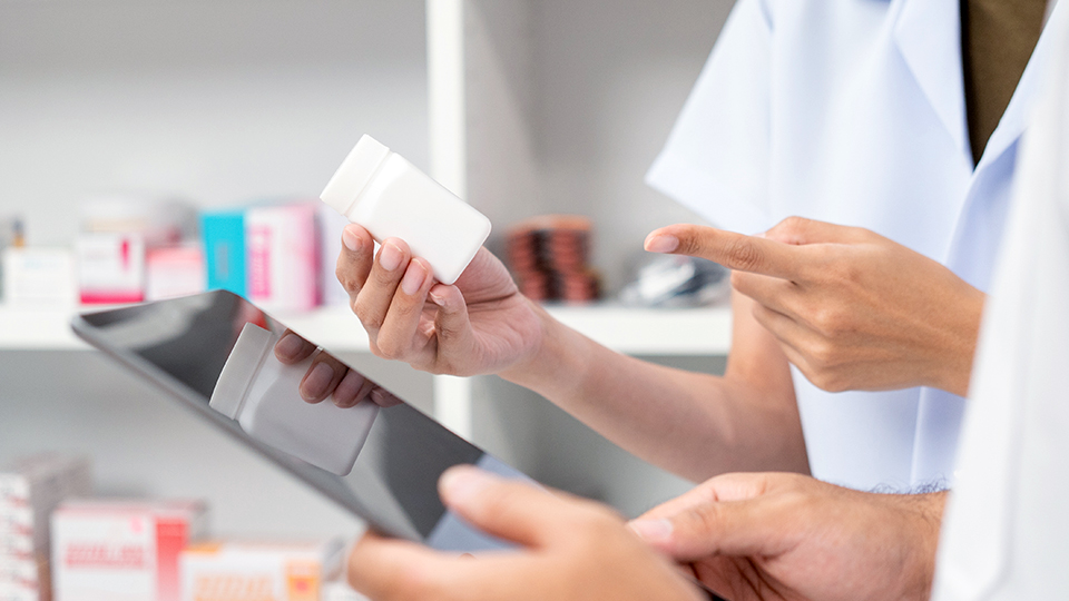 The hands of two students; one is holding a pill bottle and one is holding a tablet.
