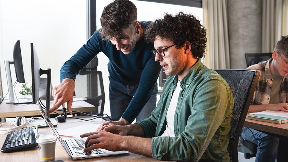 Two students collaborating on a laptop in a computer lab