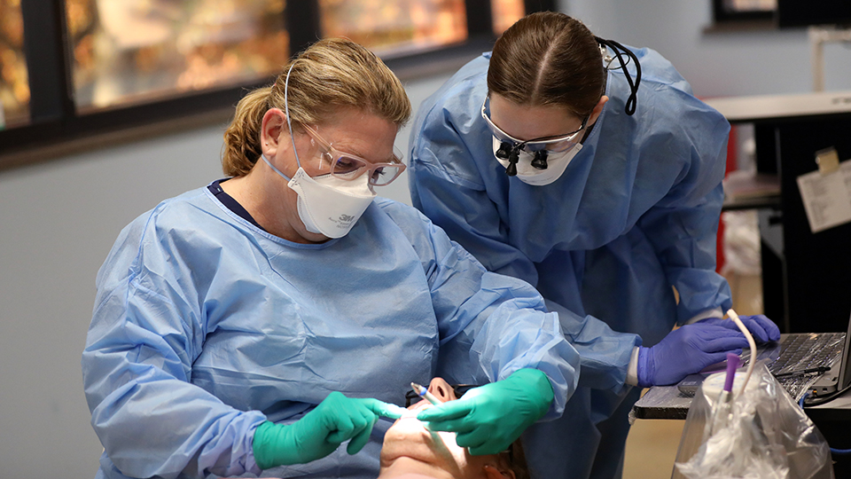 An instructor supervises a student doing a dental cleaning on a patient.