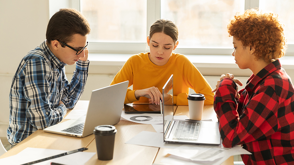 Three students working at a table, each with open laptops