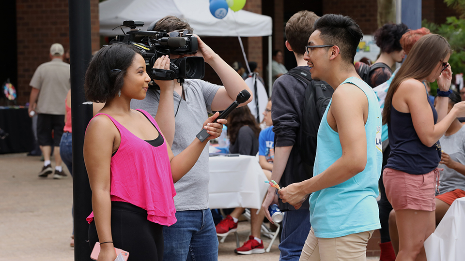 Students with a camera and microphone interview another student.