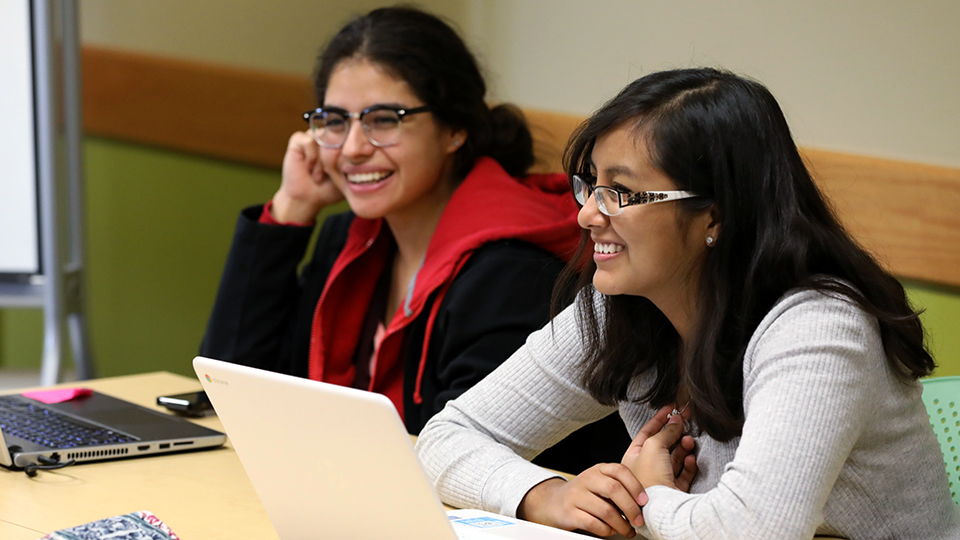 Two students at a table with laptops.