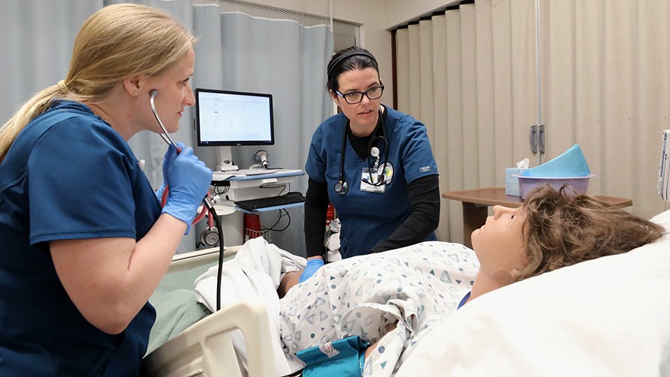 two nursing students practice skills on a simulation dummy