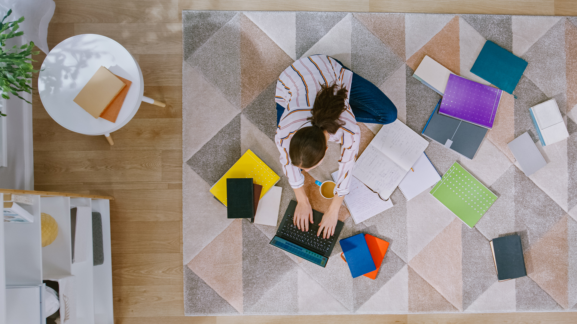 A young woman sitting on the floor in her living room using a laptop