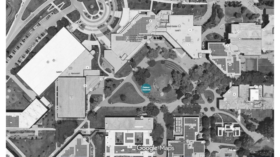 Grayscale aerial satellite map showing a section of campus with a blue circle labeled Outdoor Classroom in a grassy field south of a large parking lot.