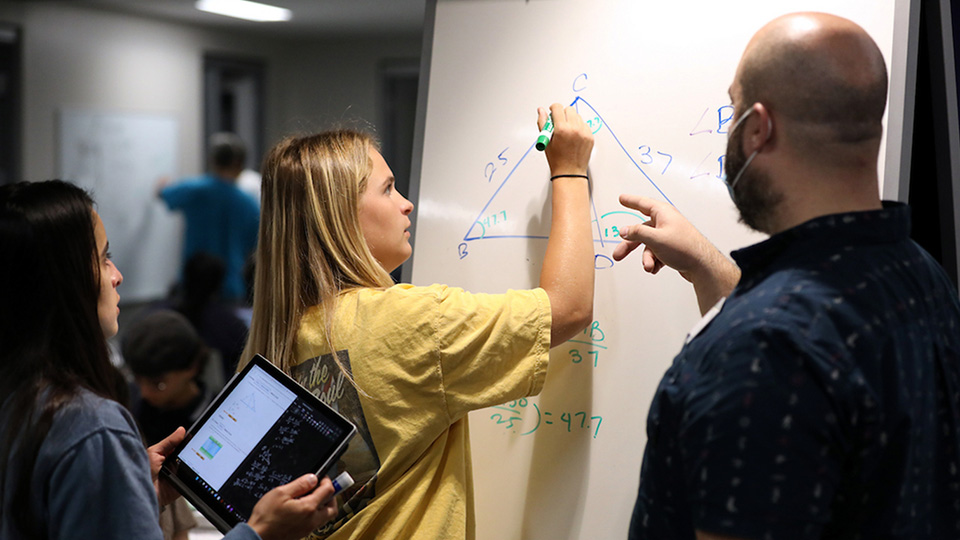 a student writes a math problem on a white board