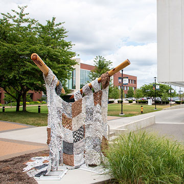 “One Stitch at a Time” by art student Alayna Reinke. The sculpture is a giant knitted afghan on giant knitting needles. The "yarn" is plastic bags.