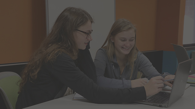 Two women look at a laptop. One is pointing at the screen.