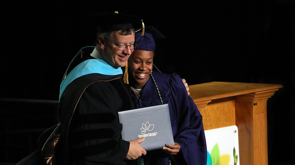 Dr. Andrew Bowne with his arm around a graduate during the graduation ceremony