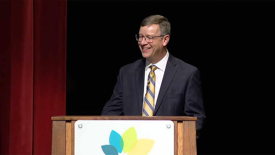 Dr. Andrew Bowne stands behind a podium and smiles