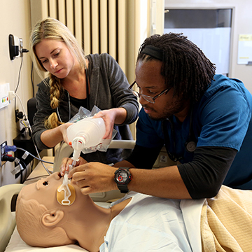 Two respiratory care students works on a manikin.