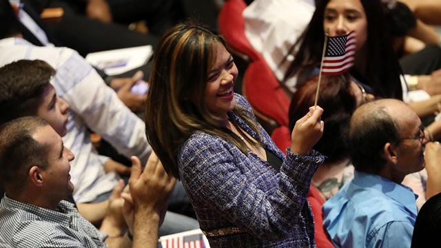 A photo of a group of adults smiling and waving an American flag at a naturalization ceremony