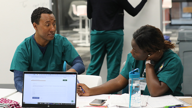 2 medical students sit at a table and work on an assignment
