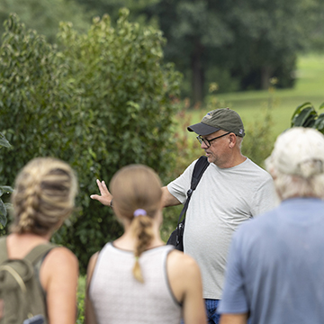 students listen and a master gardener explains about a tree in the JCCC food forest