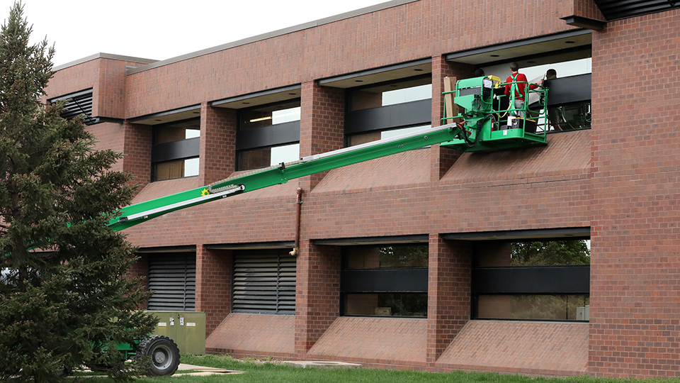 workers use a lift truck to install dots on the outside of second story windows on the JCCC campus