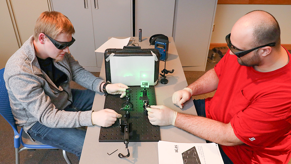 Two students wearing protective eye gear working with a laser