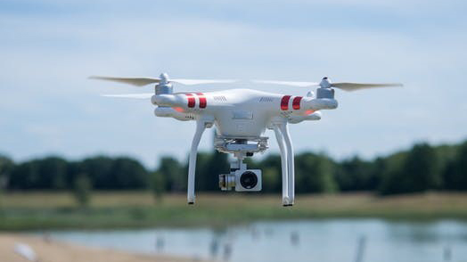 A white drone hovers over a small body of water.
