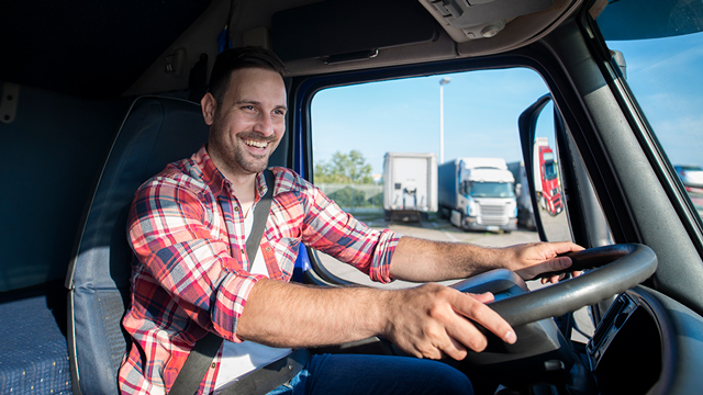 A man smiles from behind the steering wheel of a semi truck