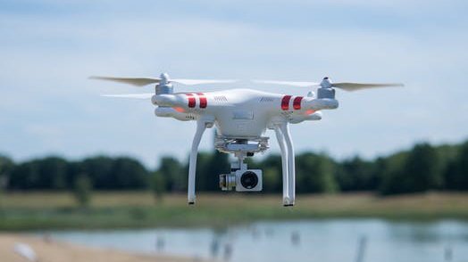A white drone hovers over a small body of water.