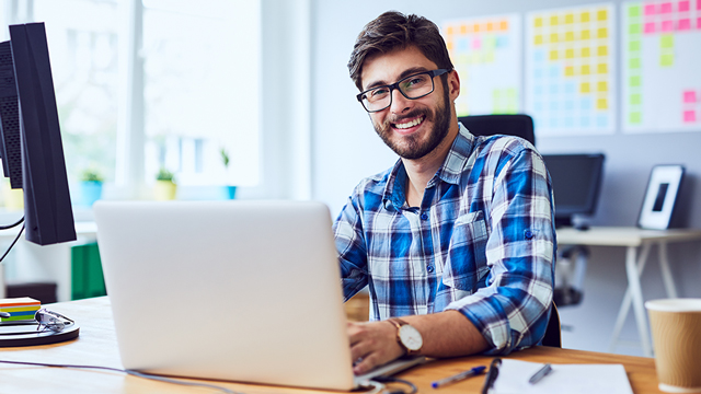 A middle-aged man smiles from behind a laptop screen.