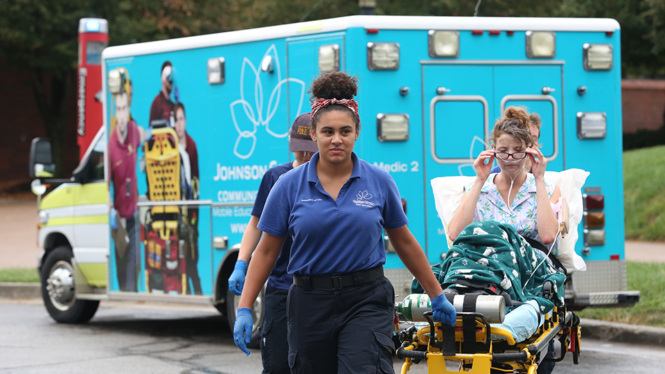 A female EMT pulls a gurney away from an ambulance.