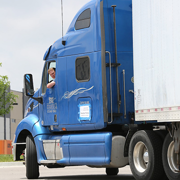A male CDL student looks out of the window of a semi truck trailer 