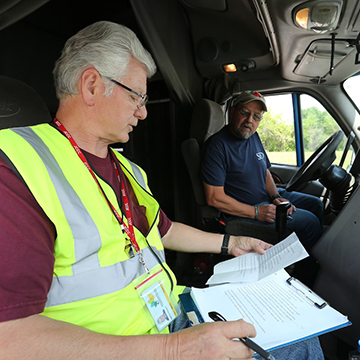 A CDL instructor goes over a checklist with a student driver while seated in the cab of a commercial truck.