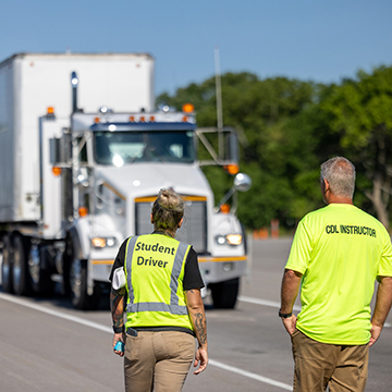 a cdl student driver and instructor watch a truck approach on the training course
