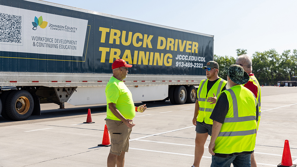 cdl students talk with an instructor in front of a tractor trailer