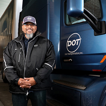 A student wearing a proud smile stands next to the cab of a commercial truck.