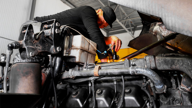 A JCCC student uses a flashlight to inspect an engine.