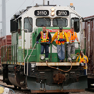 Three men stand on the front of a railcar