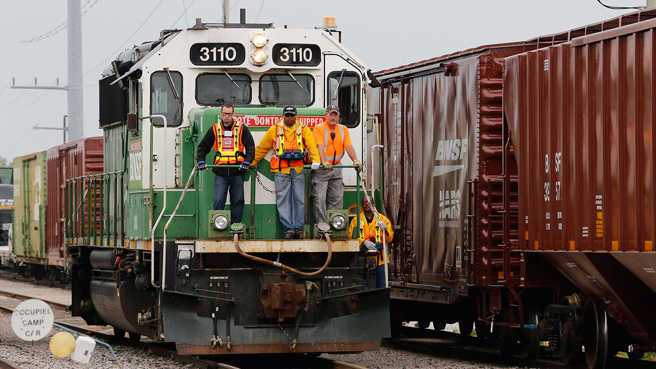 Three men ride on the front of a train car