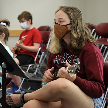 masked female student playing the ukulele
