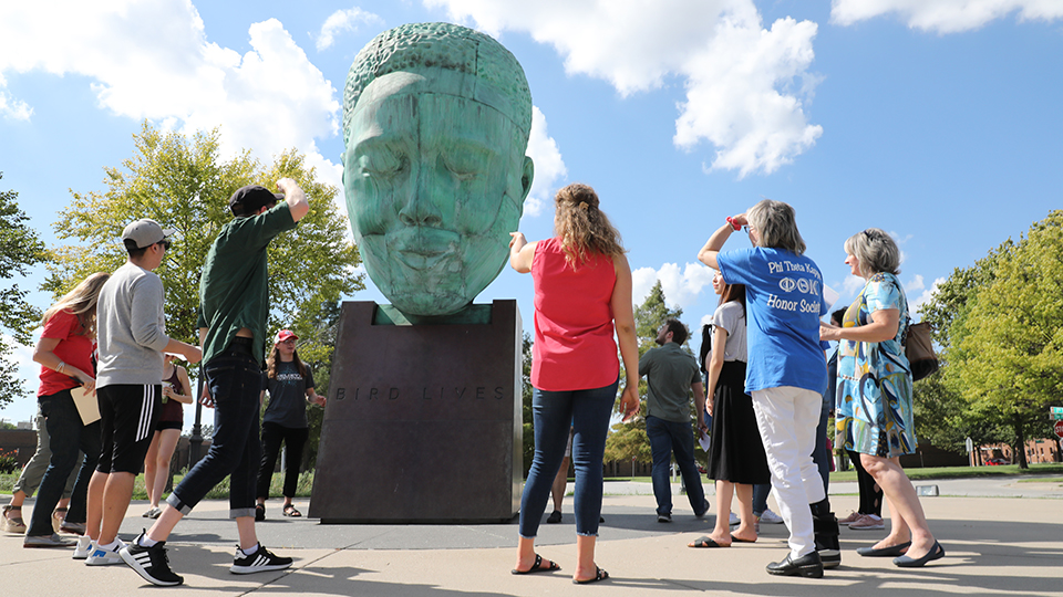 Art history students gathered around a campus sculpture